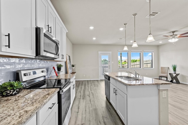 kitchen with white cabinets, appliances with stainless steel finishes, tasteful backsplash, and a kitchen island with sink