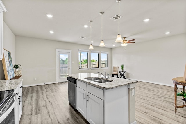 kitchen featuring appliances with stainless steel finishes, light stone counters, sink, white cabinets, and an island with sink