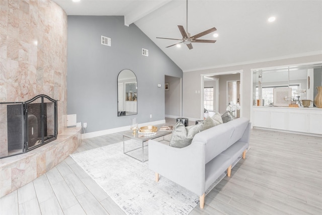 living room with high vaulted ceiling, ceiling fan, light wood-type flooring, beam ceiling, and a tiled fireplace