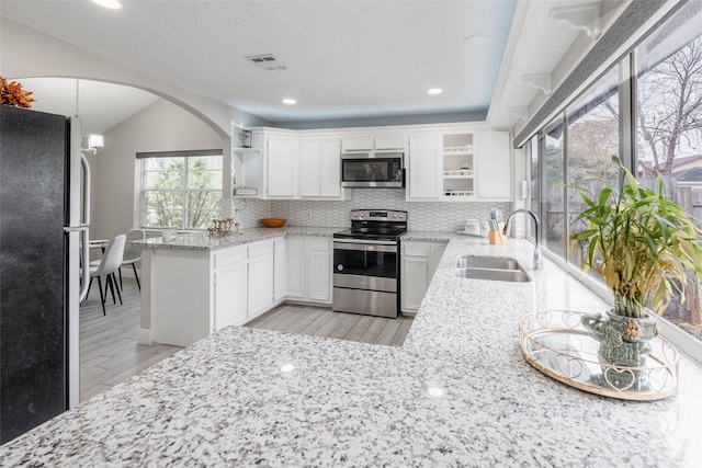 kitchen featuring kitchen peninsula, sink, appliances with stainless steel finishes, light stone counters, and white cabinetry