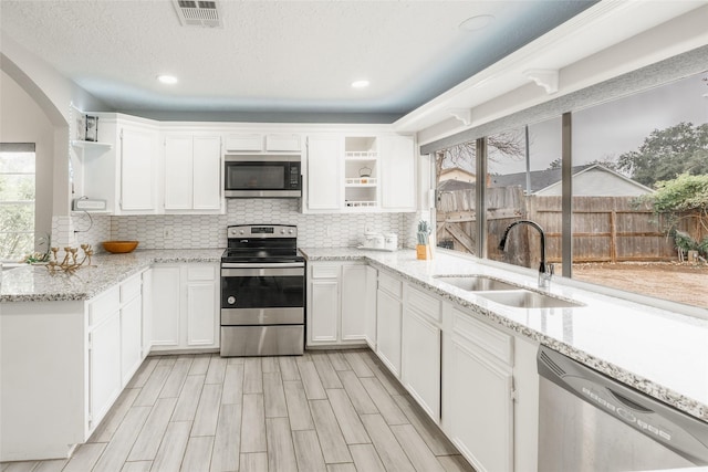 kitchen featuring white cabinets, appliances with stainless steel finishes, light stone countertops, and sink