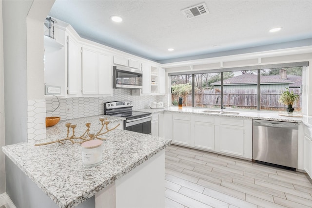 kitchen with white cabinets, sink, light stone countertops, appliances with stainless steel finishes, and kitchen peninsula