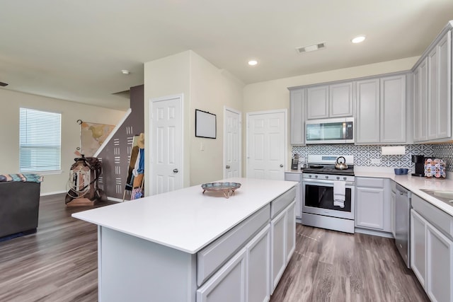 kitchen featuring wood-type flooring, stainless steel appliances, a kitchen island, and gray cabinetry