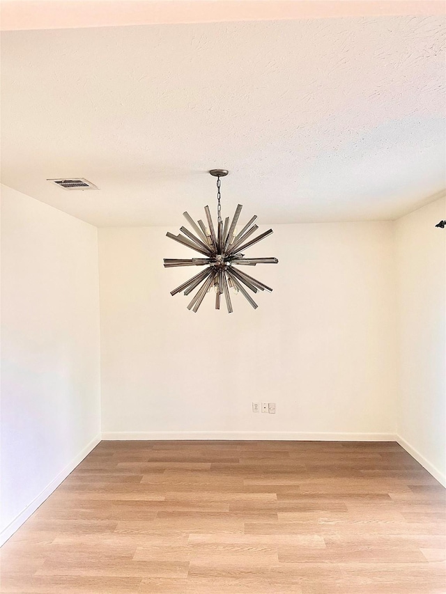 empty room featuring light wood-type flooring, a textured ceiling, and a chandelier