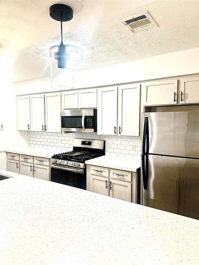 kitchen featuring pendant lighting, backsplash, appliances with stainless steel finishes, and a textured ceiling