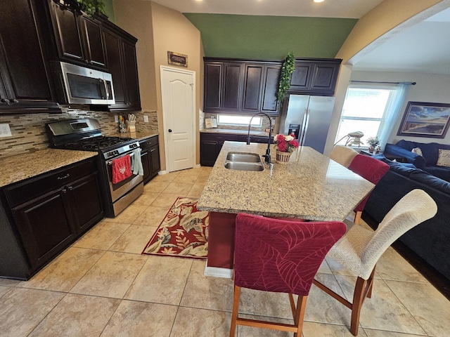 kitchen with sink, a breakfast bar, backsplash, stainless steel appliances, and an island with sink