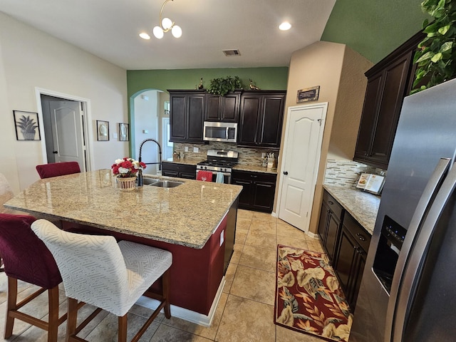 kitchen featuring appliances with stainless steel finishes, an island with sink, sink, a breakfast bar area, and light stone countertops