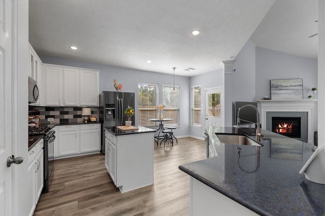 kitchen with black gas range, a center island with sink, hanging light fixtures, decorative backsplash, and white cabinetry