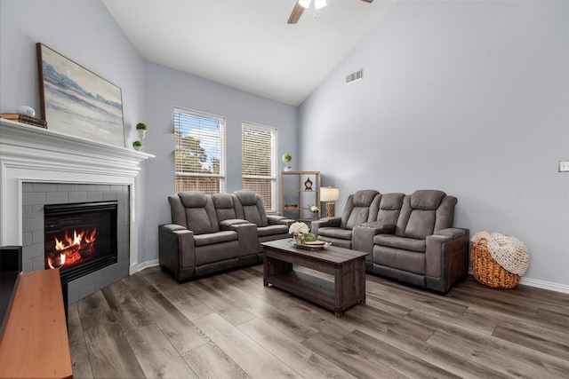 living room featuring hardwood / wood-style flooring, ceiling fan, high vaulted ceiling, and a tile fireplace