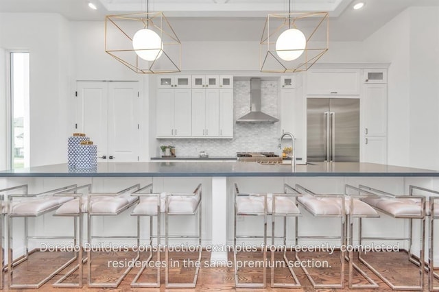 kitchen featuring stainless steel built in fridge, decorative light fixtures, white cabinetry, and wall chimney exhaust hood