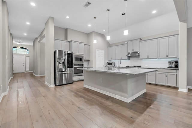 kitchen featuring light stone countertops, appliances with stainless steel finishes, pendant lighting, a high ceiling, and an island with sink