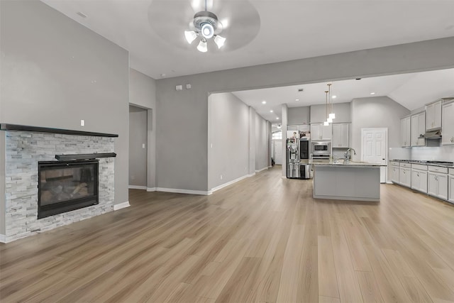 kitchen with sink, an island with sink, decorative light fixtures, a fireplace, and appliances with stainless steel finishes