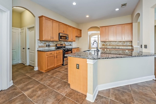 kitchen featuring decorative backsplash, appliances with stainless steel finishes, kitchen peninsula, sink, and dark stone countertops