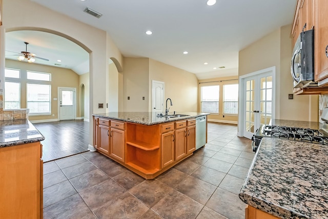 kitchen with french doors, sink, stainless steel dishwasher, dark stone countertops, and an island with sink