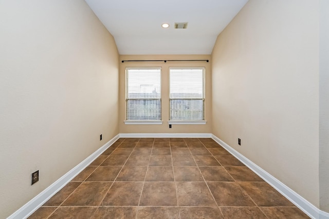 spare room featuring dark tile patterned floors and vaulted ceiling