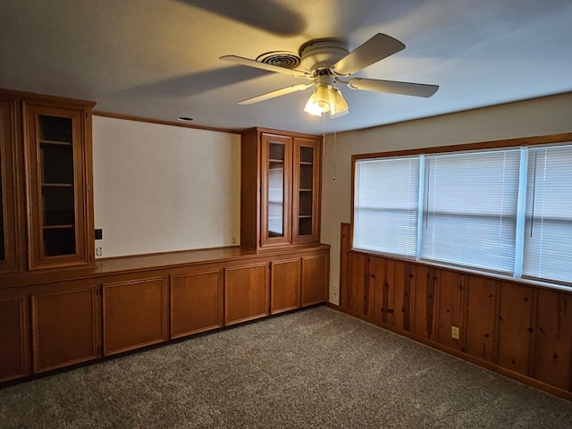 carpeted empty room with ceiling fan and wood walls