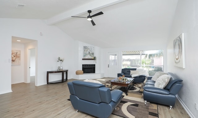 living room with ceiling fan, a fireplace, lofted ceiling with beams, and light wood-type flooring