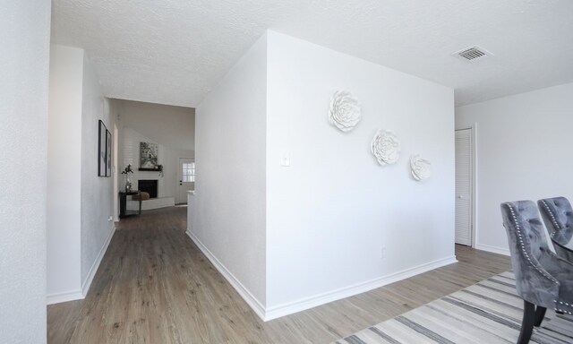 corridor with a textured ceiling and light hardwood / wood-style flooring