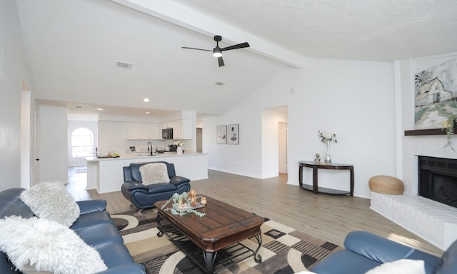 living room featuring lofted ceiling with beams, sink, light hardwood / wood-style flooring, ceiling fan, and a fireplace