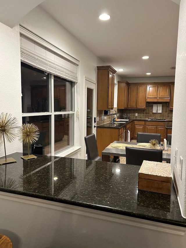 kitchen featuring decorative backsplash, sink, kitchen peninsula, and dark stone countertops