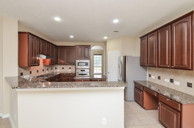 kitchen with kitchen peninsula, appliances with stainless steel finishes, light tile patterned floors, and dark stone counters