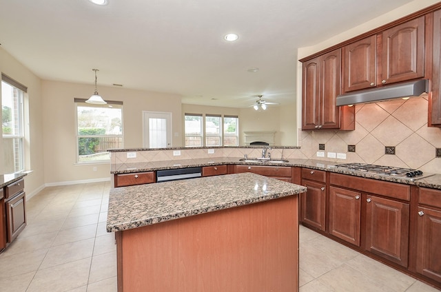 kitchen with a center island, sink, hanging light fixtures, stainless steel gas cooktop, and light stone counters