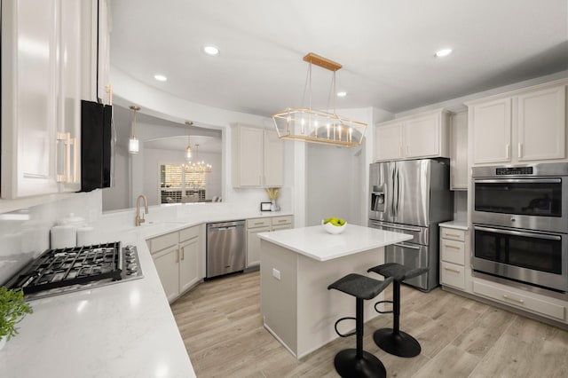 kitchen with white cabinetry, light hardwood / wood-style flooring, decorative light fixtures, a breakfast bar, and appliances with stainless steel finishes