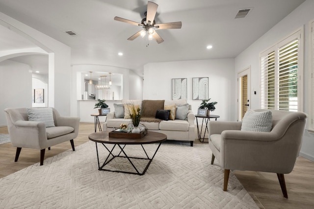 living room with ceiling fan with notable chandelier and light hardwood / wood-style floors