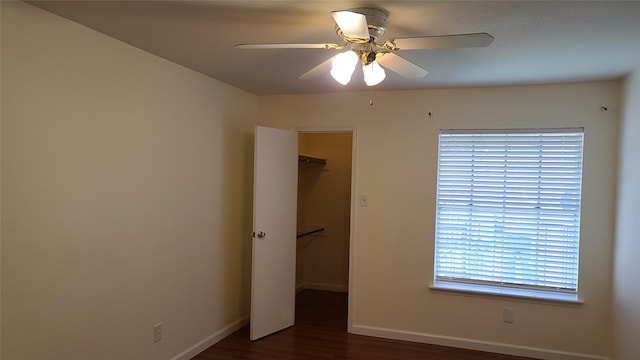 unfurnished bedroom featuring ceiling fan, dark hardwood / wood-style floors, a walk in closet, and a closet