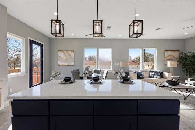 kitchen featuring plenty of natural light, light stone countertops, decorative light fixtures, and light hardwood / wood-style flooring