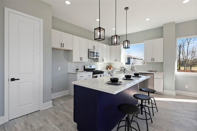 kitchen with a kitchen bar, appliances with stainless steel finishes, light wood-type flooring, a kitchen island, and white cabinetry