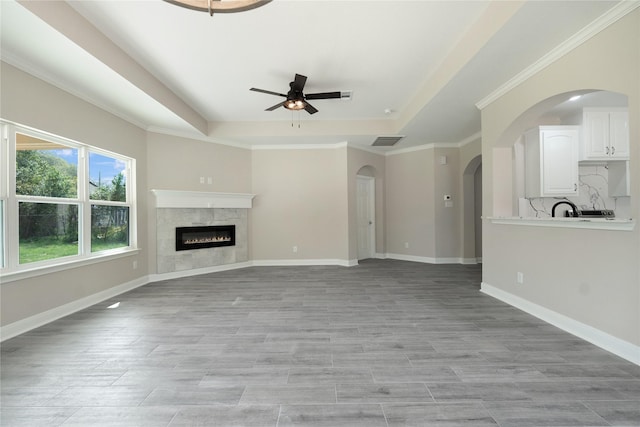 unfurnished living room featuring ceiling fan, a premium fireplace, light hardwood / wood-style flooring, and a tray ceiling