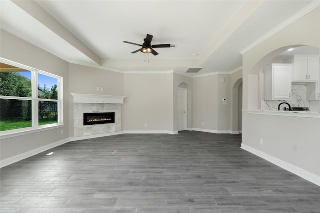 unfurnished living room with a high end fireplace, a raised ceiling, and ceiling fan