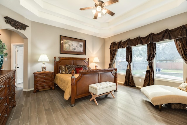 bedroom with hardwood / wood-style floors, ceiling fan, and a tray ceiling