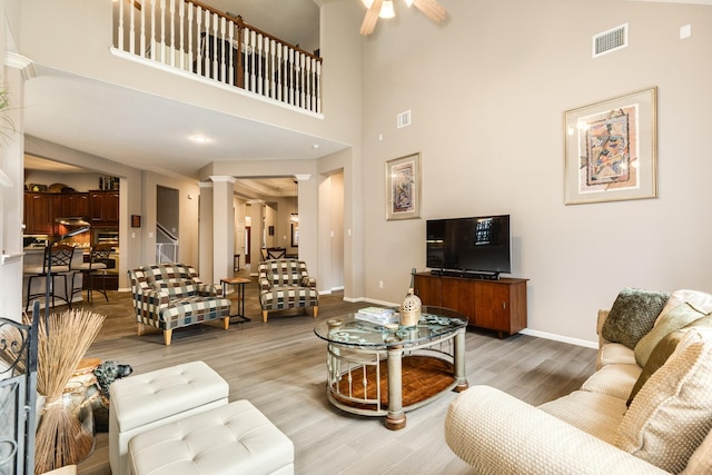 living room with wood-type flooring, a towering ceiling, ornate columns, and ceiling fan