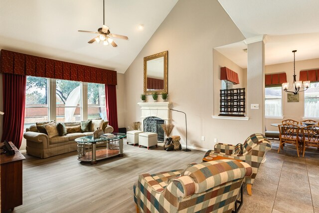 living room with light wood-type flooring, ceiling fan with notable chandelier, and high vaulted ceiling