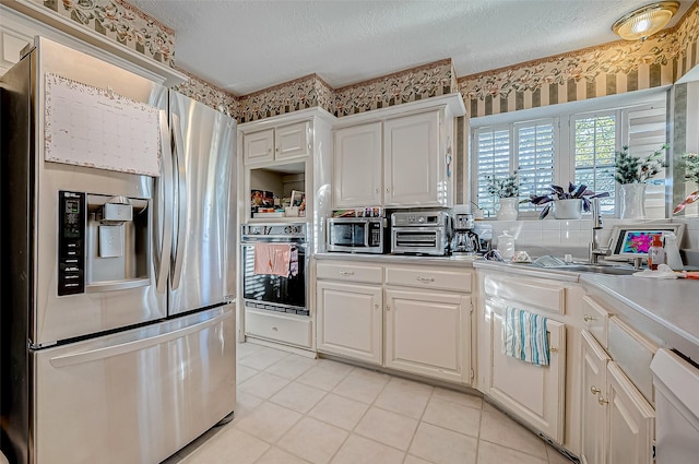 kitchen featuring appliances with stainless steel finishes, light tile patterned floors, a textured ceiling, and white cabinetry