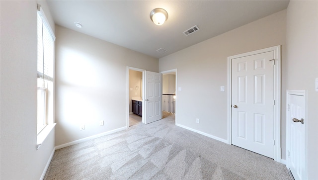 unfurnished bedroom featuring multiple windows, ensuite bath, and light carpet