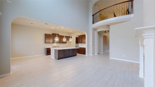 kitchen with hanging light fixtures, a center island, light wood-type flooring, and a towering ceiling