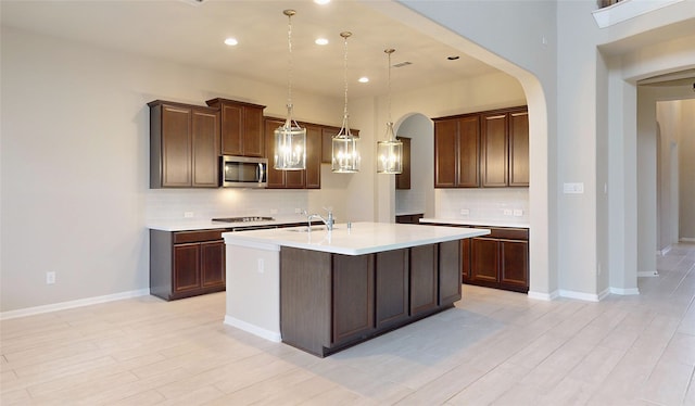 kitchen with pendant lighting, sink, a kitchen island with sink, black gas cooktop, and decorative backsplash