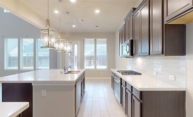 kitchen with sink, hanging light fixtures, dark brown cabinetry, stainless steel appliances, and a center island with sink