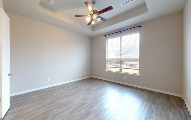 spare room with ceiling fan, a tray ceiling, and light hardwood / wood-style flooring