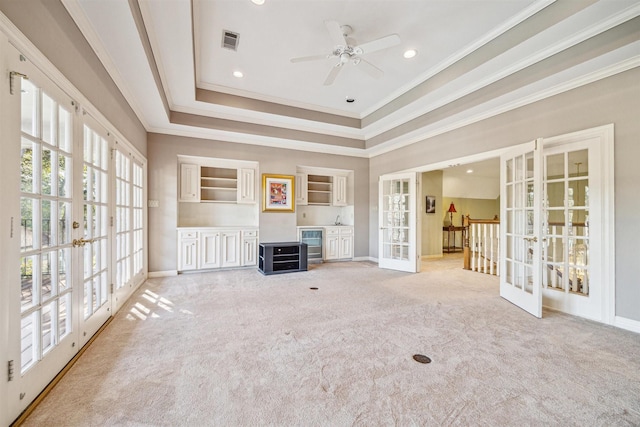 unfurnished living room featuring french doors, a tray ceiling, light colored carpet, beverage cooler, and crown molding