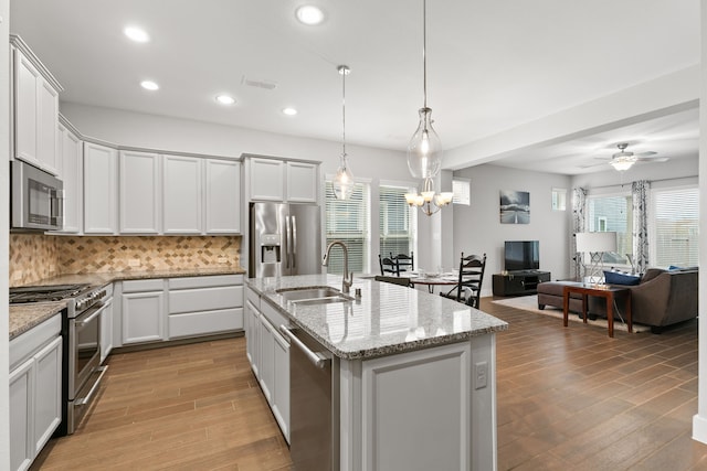 kitchen with a center island with sink, sink, hanging light fixtures, decorative backsplash, and appliances with stainless steel finishes