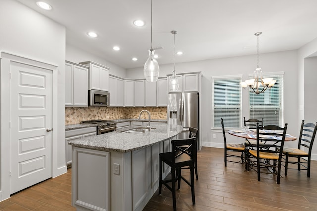 kitchen with pendant lighting, a center island with sink, sink, tasteful backsplash, and stainless steel appliances