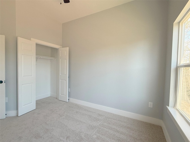 unfurnished bedroom featuring ceiling fan, multiple windows, a closet, and light carpet