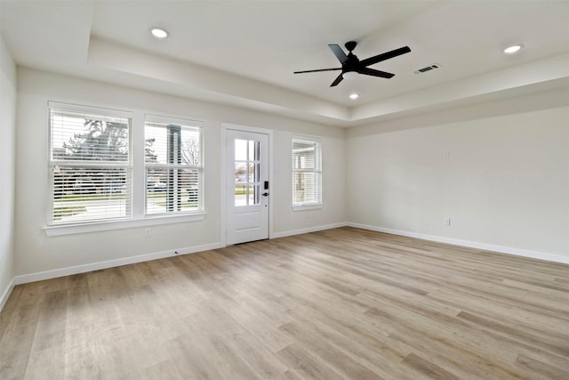 spare room featuring a tray ceiling, ceiling fan, and light hardwood / wood-style floors