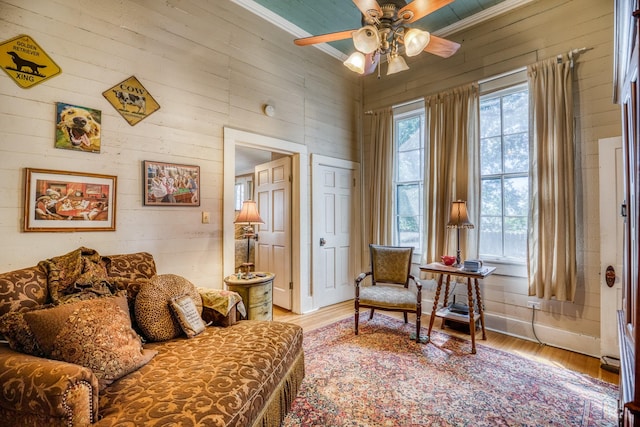 sitting room featuring wood-type flooring, ceiling fan, crown molding, and wood walls