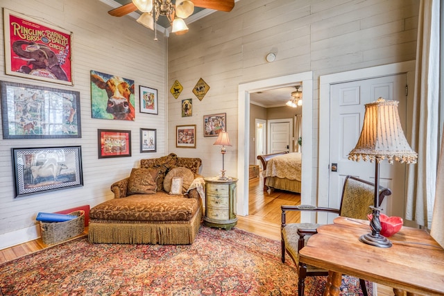 living area with ceiling fan, hardwood / wood-style floors, crown molding, and wooden walls