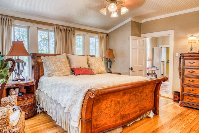 bedroom with multiple windows, ceiling fan, light hardwood / wood-style flooring, and wood walls